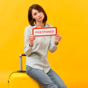 woman-standing-her-luggage-while-holding-postponed-sign
